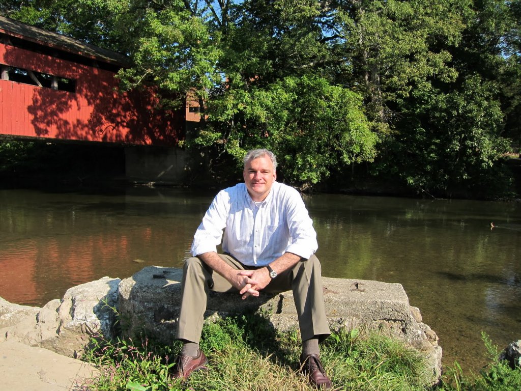John Fea sitting on a rock at the edge of a small river