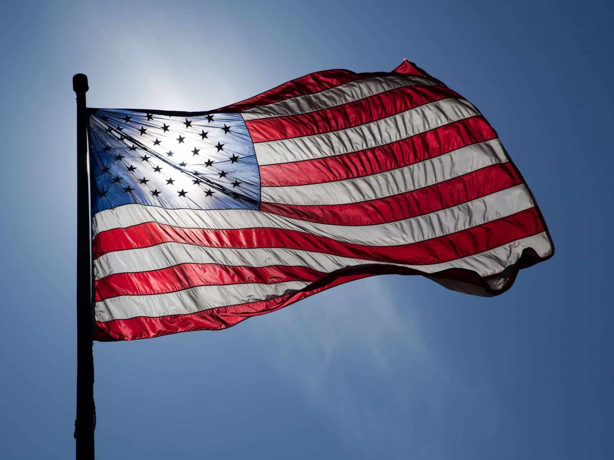 American flag waving in the wind with the sun shining through it.