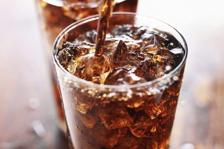 Image shows a glass of ice with brown soda being toped off.
