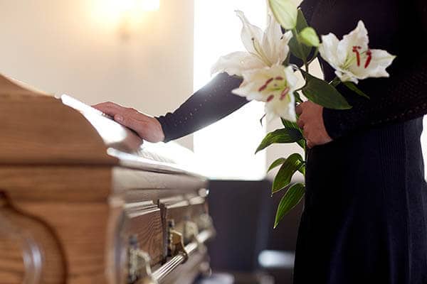 My friend wasn't supposed to die A woman dressed in black is shown with a hand on a casket and holding a bouquet of white flowers.