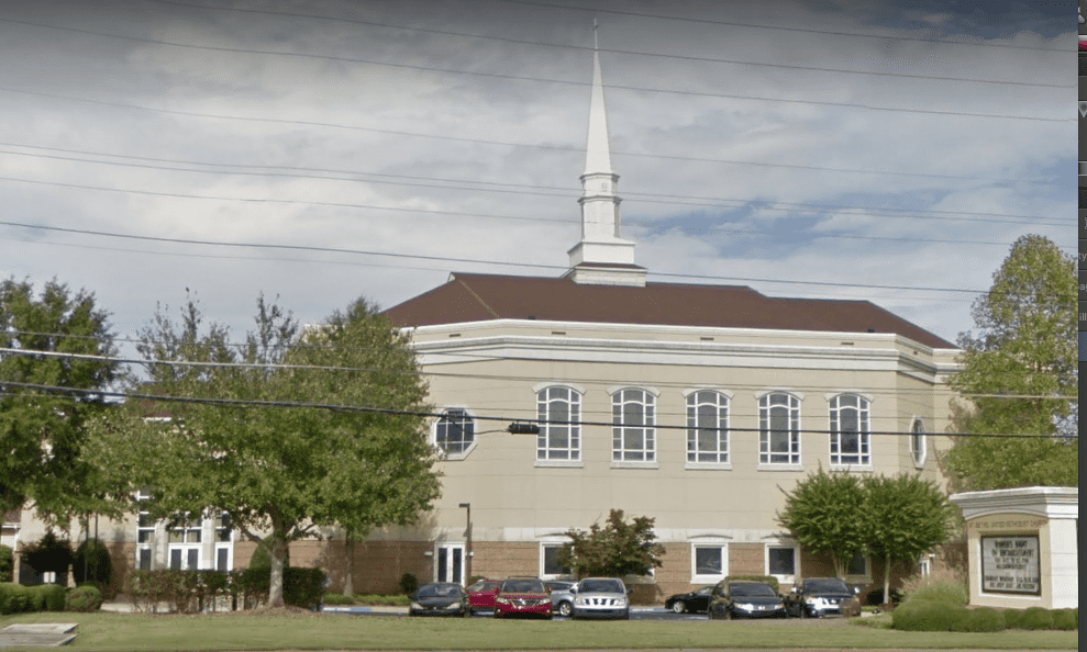 View of the side of a church with a spire from the road.