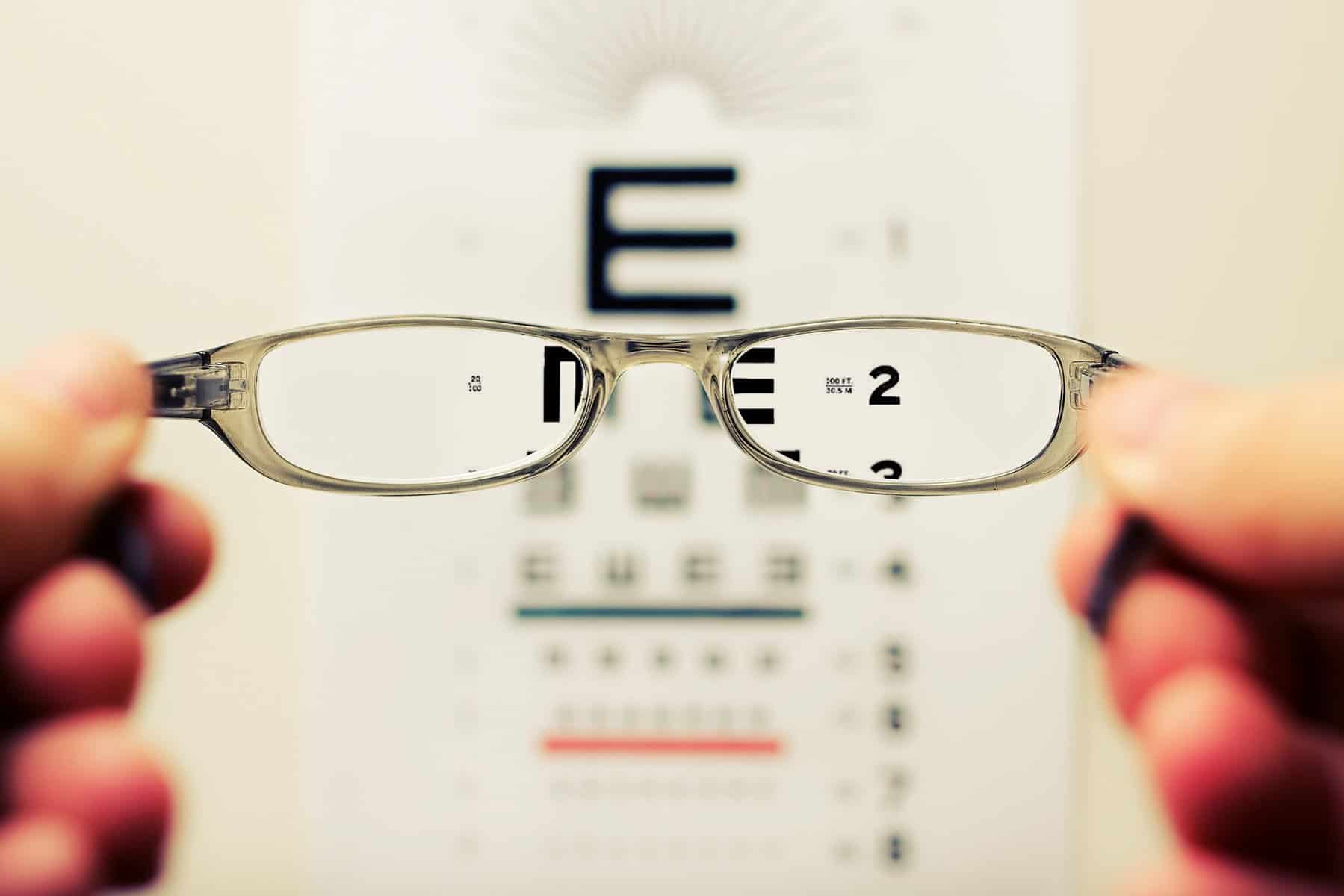 Eyeglasses are held in front of an eye exam chart.