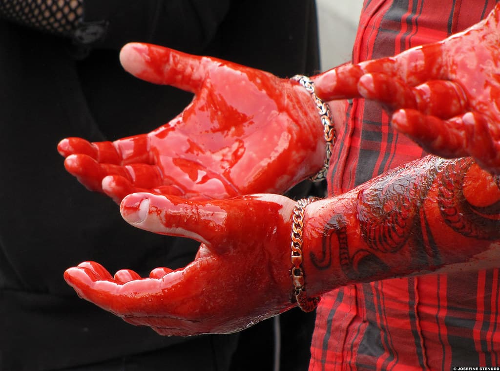 Baptizing with fake blood and blasphemy, band grabs audience attention photo of a white man's hands covered in fake blood and held in front of his red and black plaid shirt