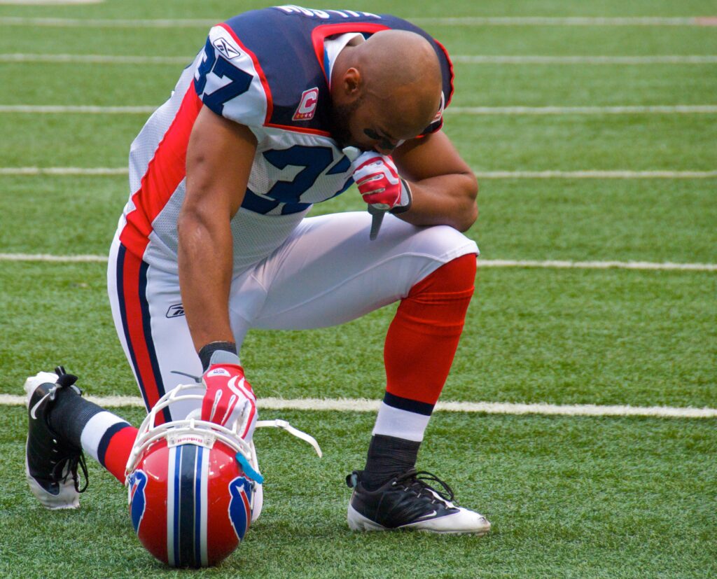 George Wilson of the Buffalo Bulls kneels with head bowed on football field in full uniform