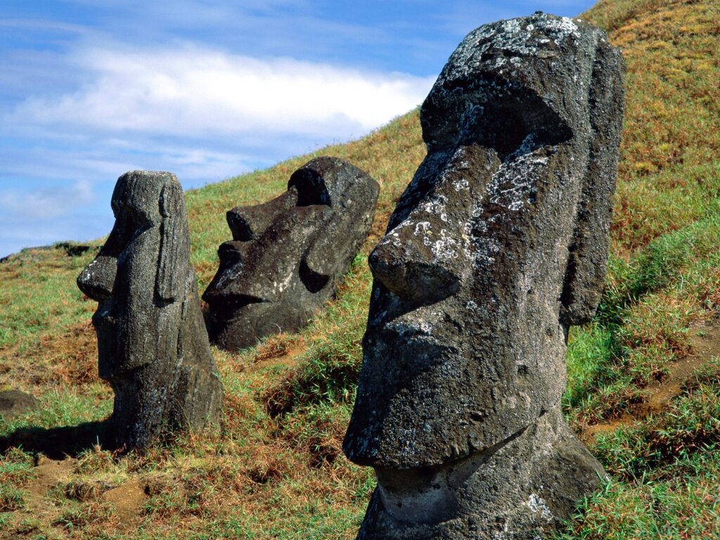 Moai monuments suffer irreparable damage Easter Island Moai monuments are shown on a grassy slope with a blue sky with a soft white cloud above