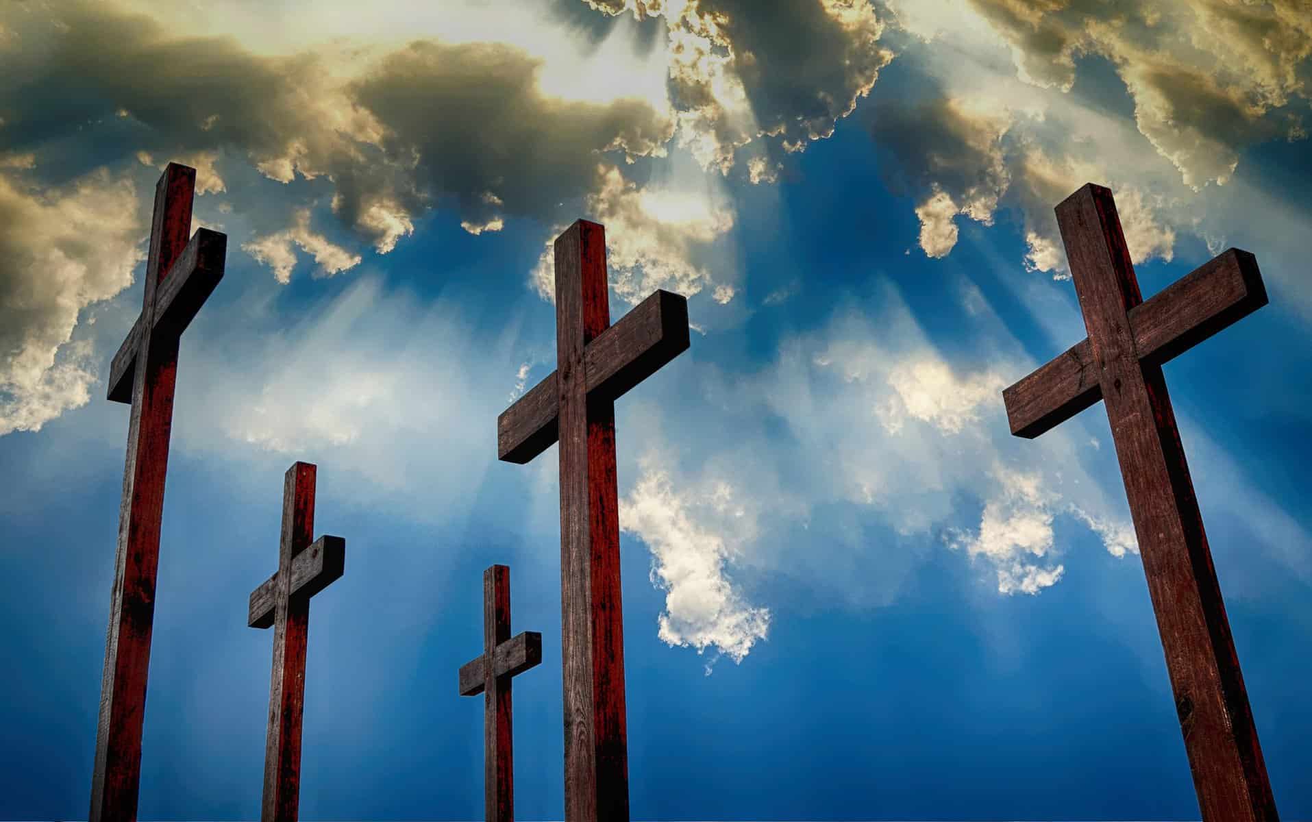 five staggered wooden crosses with a blue sky with clouds and sun rays