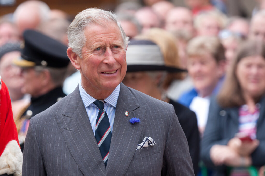 King Charles III uses first Christmas speech to pay tribute to Queen Elizabeth II King Charles is shown in a crowd wearing a gray suit with a blue flower in his lapel.