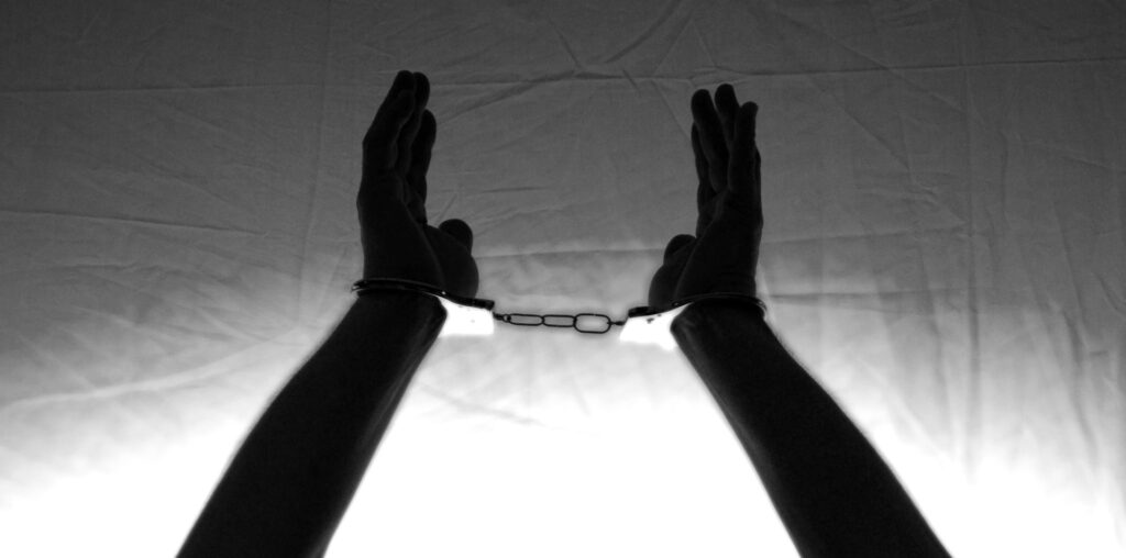 Pastor arrested in Sudan after praying for sick mother A person's hands and forearms are shown in black and white, lifted high. The wrist's are handcuffed.