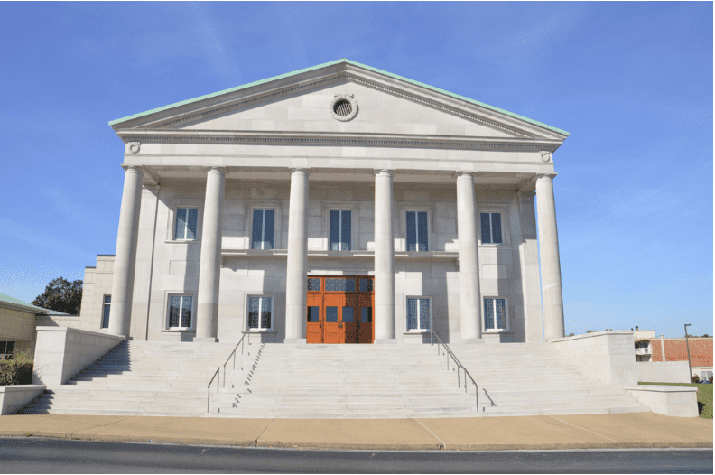 The front of a stone courthouse building is seen from the street at the top of many steps.