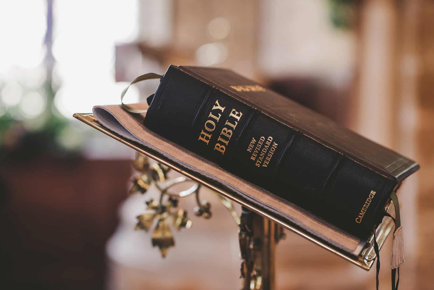 A closed black bible sits on a metal altar bookstand with the binding to the camera.