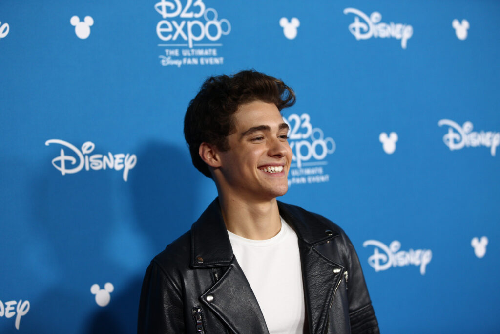Actor Joshua Bassett stands in front of company's logo's for a photo op.