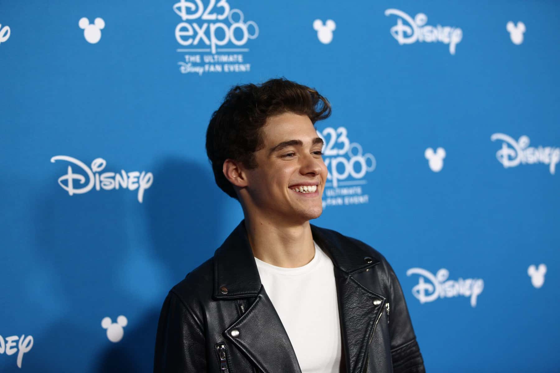 Actor Joshua Bassett stands in front of company's logo's for a photo op.