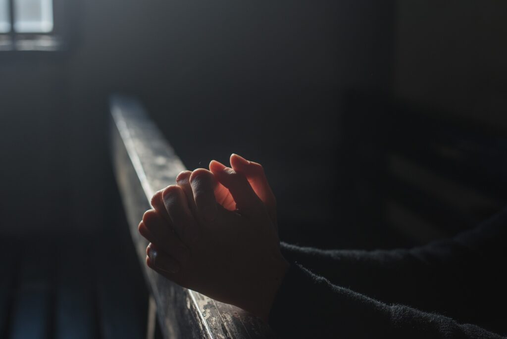 Pandemic resulted in making Americans ‘more open to God’: Study Hands are clasped in prayer at an altar rail with sunlight backlighting them through a window.