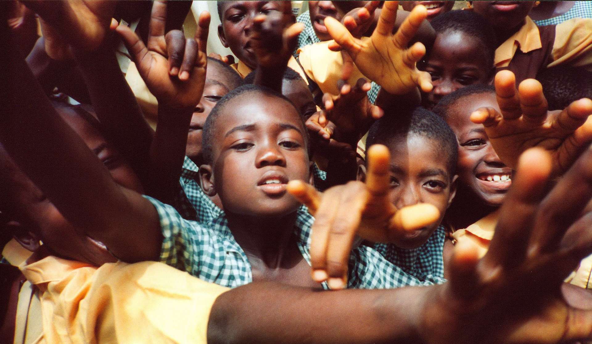 Black children as seen in a tight group from above around the camera and reaching toward it.