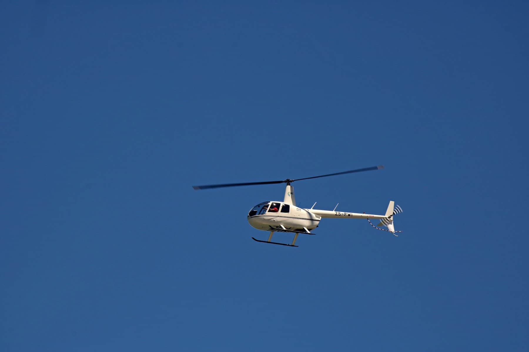 A commercial helicopter is shown high up against a blue sky.