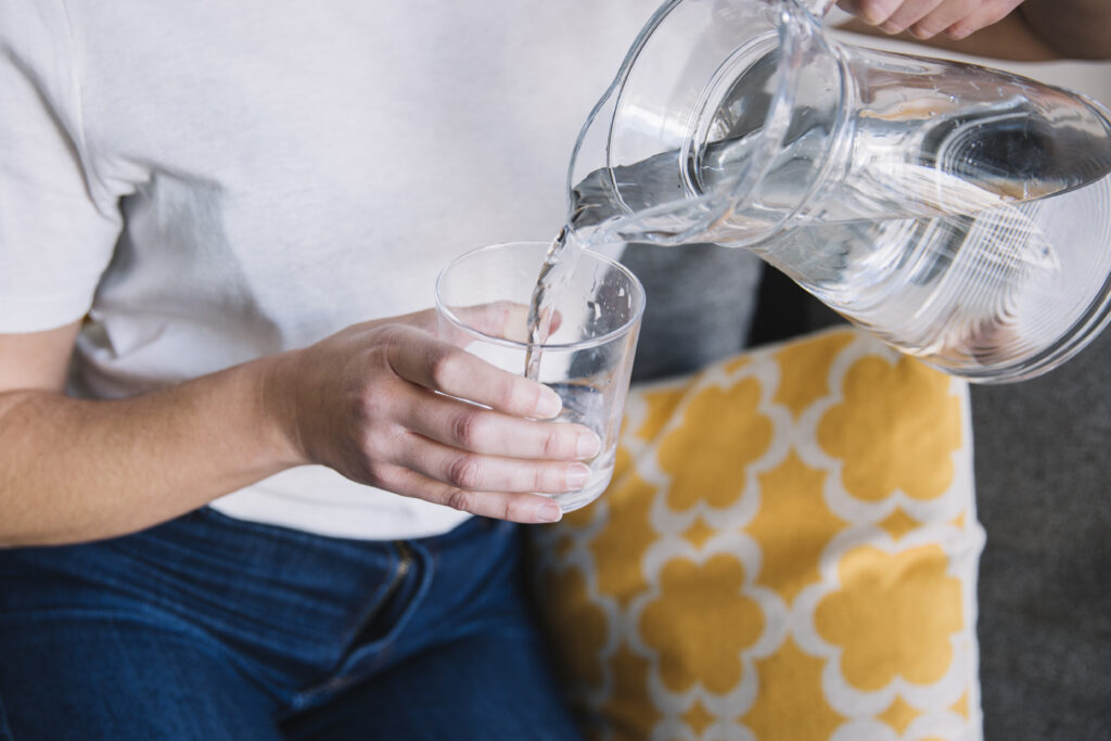 Water is shown being poured out of a clear pitcher into a clear glass.
