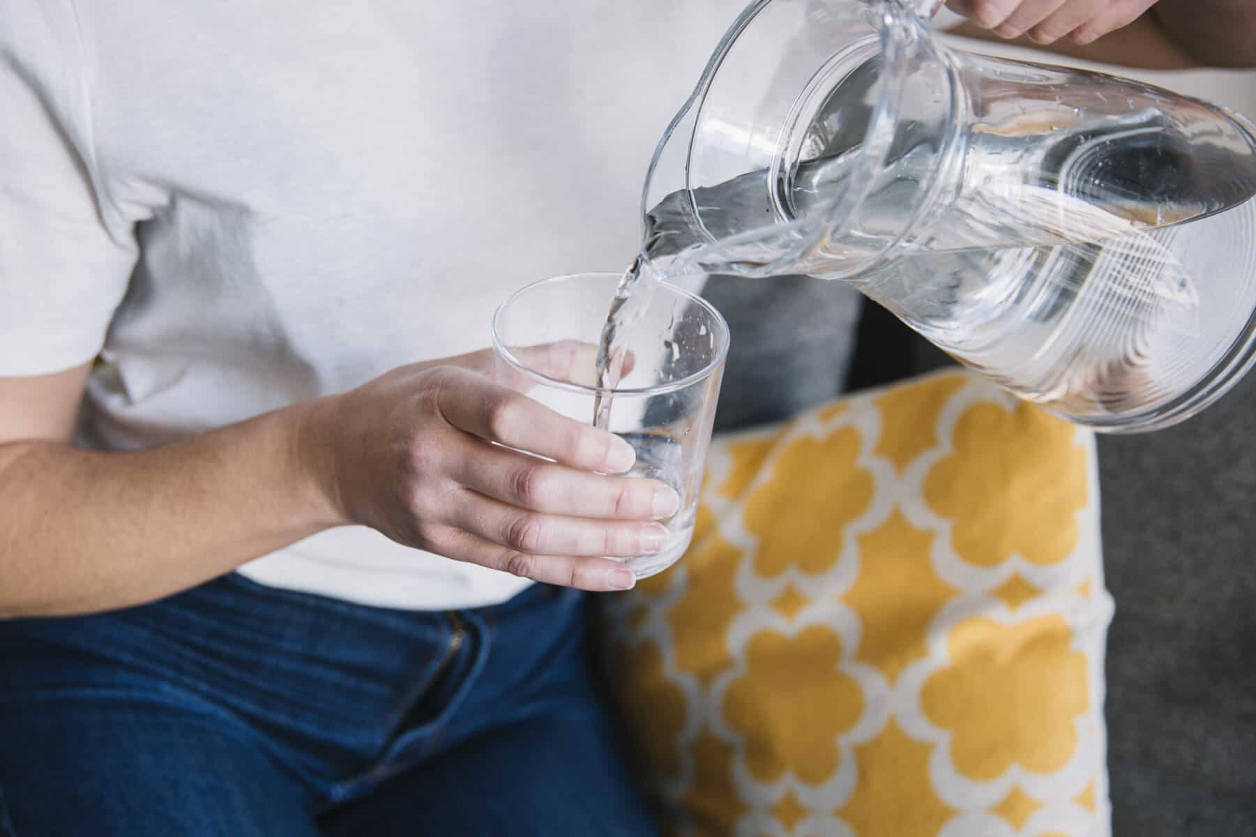Water is shown being poured out of a clear pitcher into a clear glass.