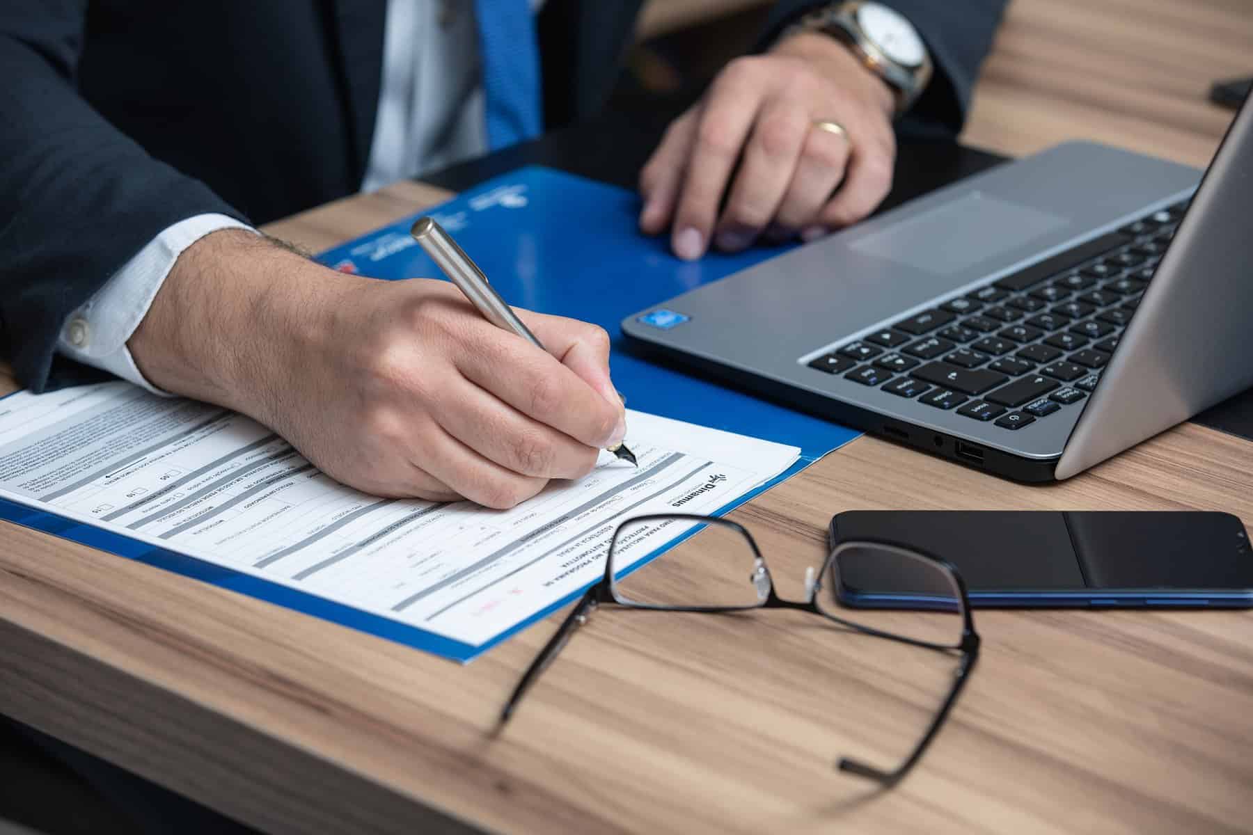 A man in a suit sits at a laptop filling out paperwork.