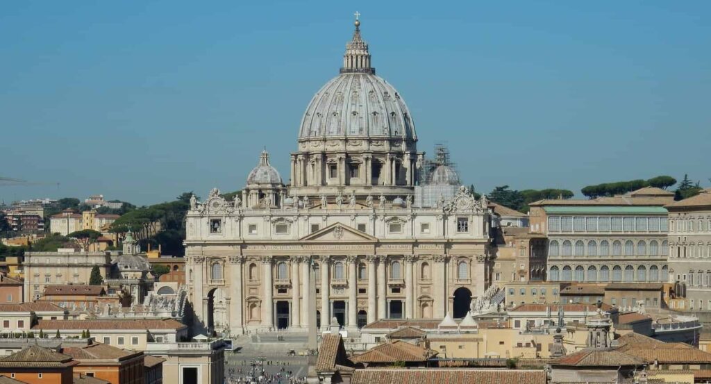 The Vatican building and dome is shown from a distance on e a slightly smoggy day.