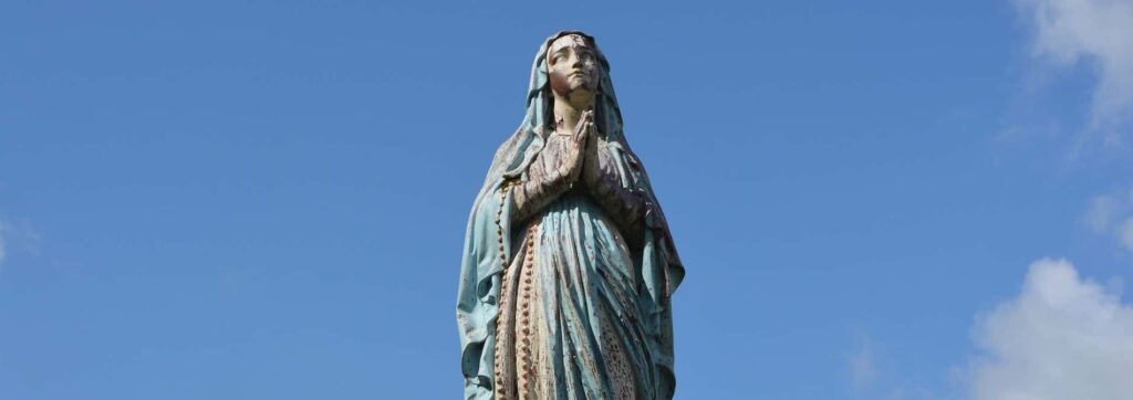 A bronze statue of the virgin Mary is seen from below and against a blue sky.
