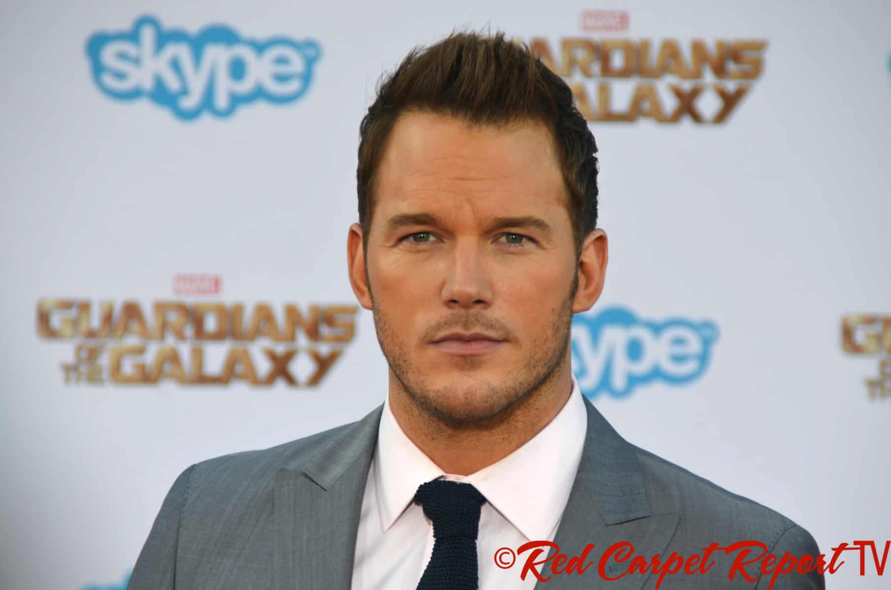 Actor Christ Pratt is shown in a grey suit with an unsmiling face.