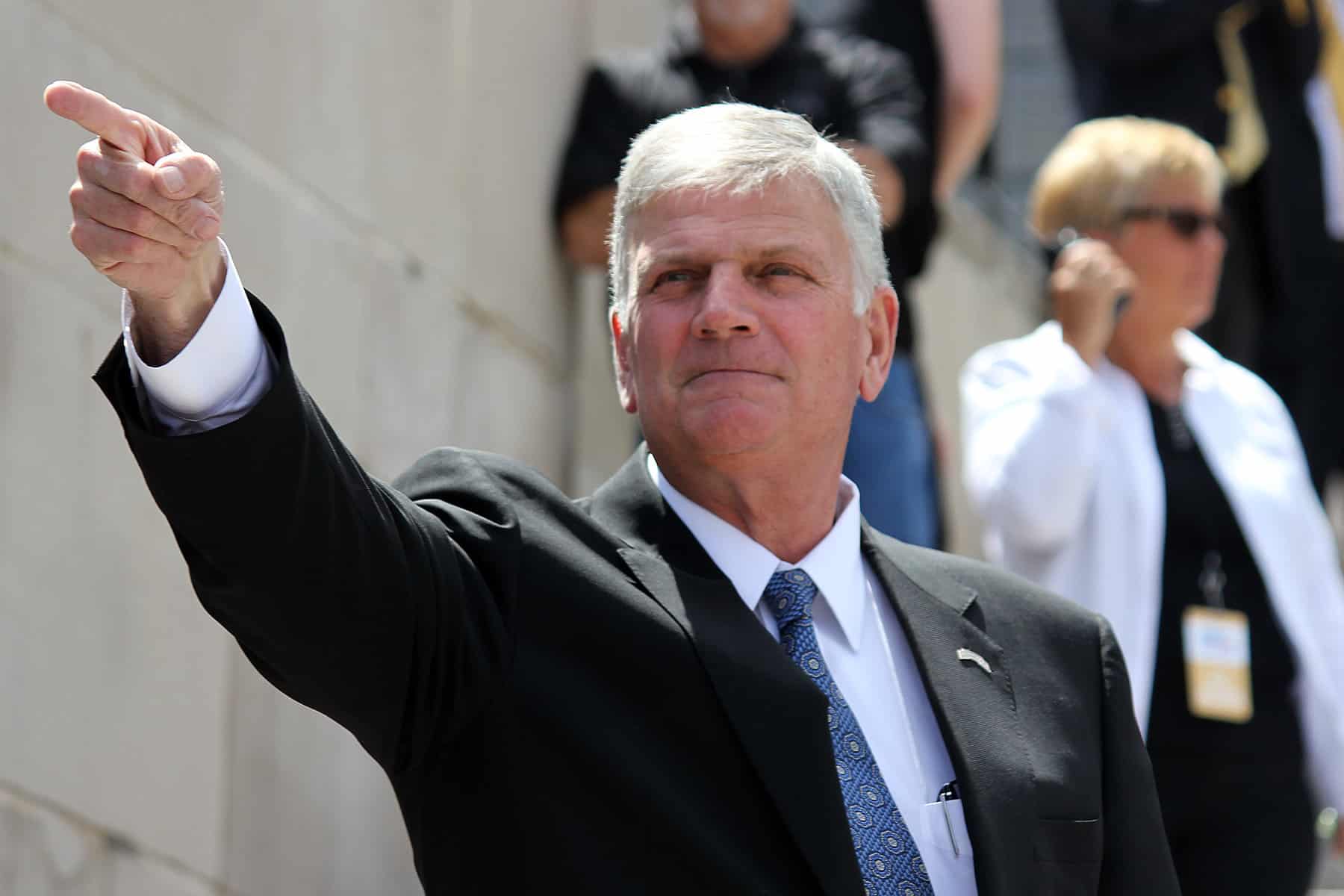 Franklin Graham is shown in a suit with an arm extended to a pointing finger.