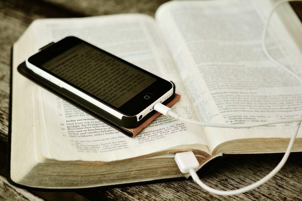A smart phone is seen sitting on a bible with its cord appearing to be plugged into the open bible.