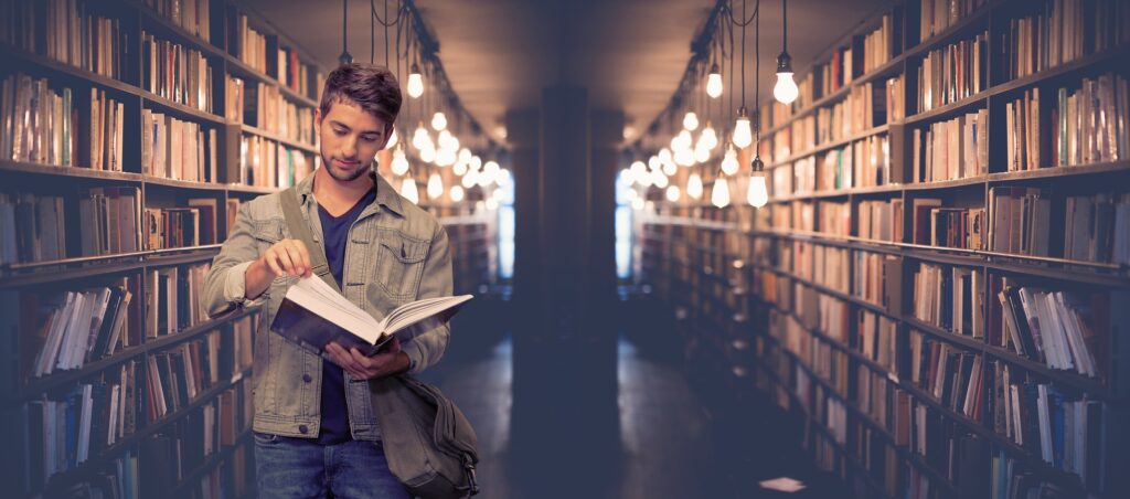 A man is seen looking through a book in a dimly lit. moody library aisle.
