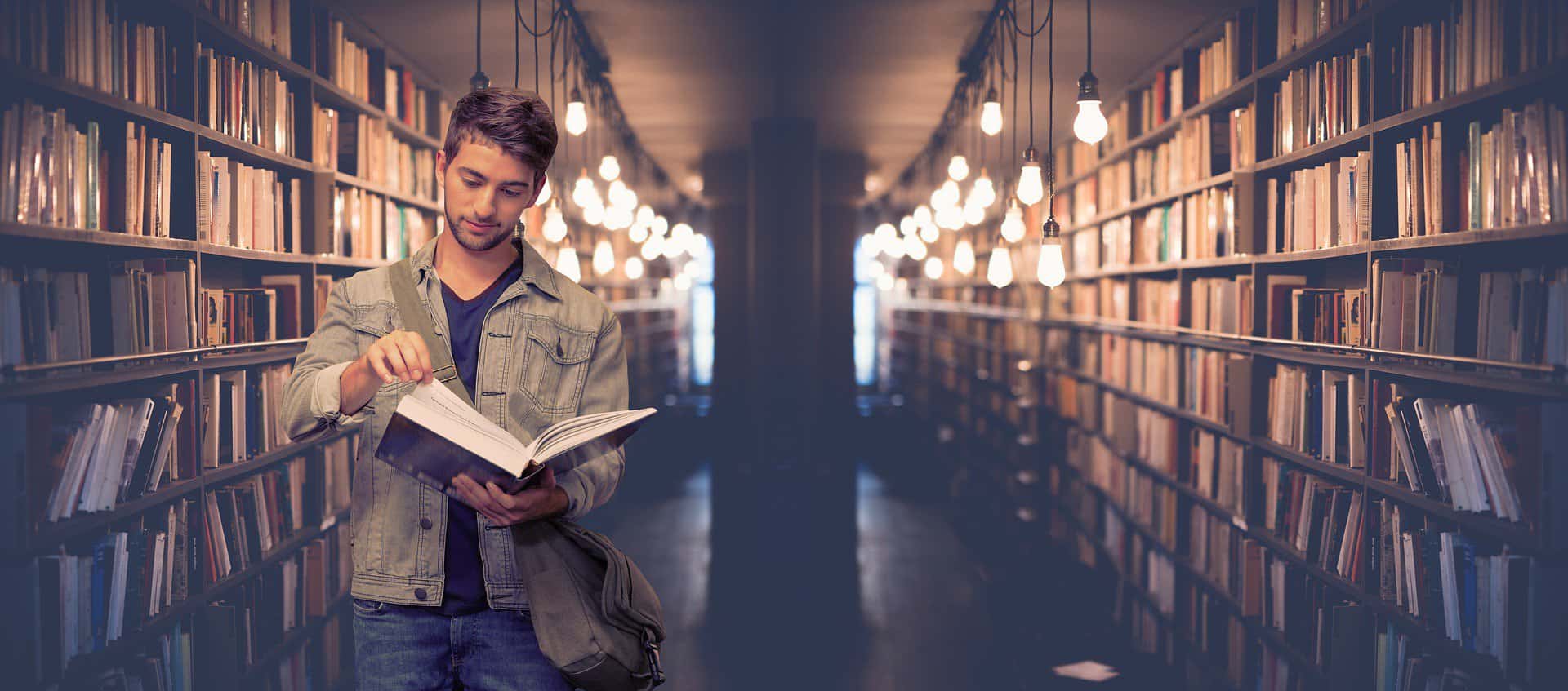 A man is seen looking through a book in a dimly lit. moody library aisle.