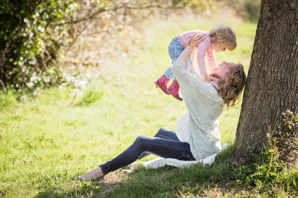 Guadalupe Project assists Catholic university moms A woman is shown sitting against a tree and holding a toddler up in the air and both are smiling.
