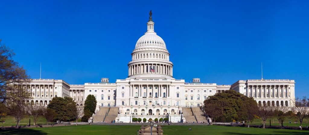 The US Capitol building is shown from far away against a blue sky with the dome in the middle.