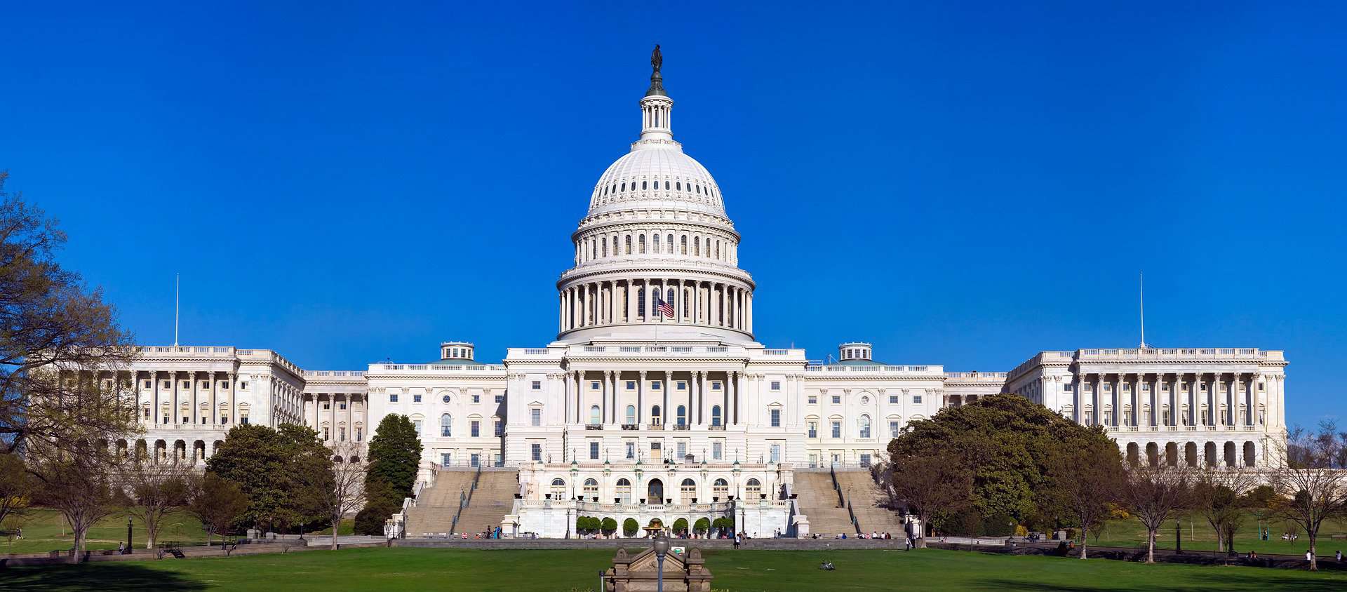 The US Capitol building is shown from far away against a blue sky with the dome in the middle.
