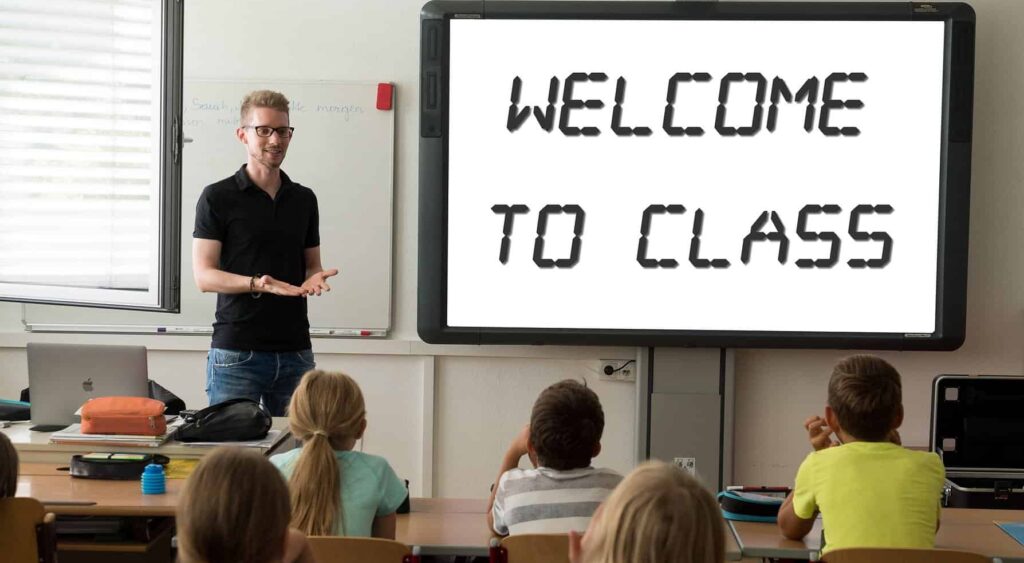 Arizona school board settles to avoid lawsuit for rejecting Christian teachers A male teacher stands at the front of a classroom of children with a sign saying "Welcome to Class".