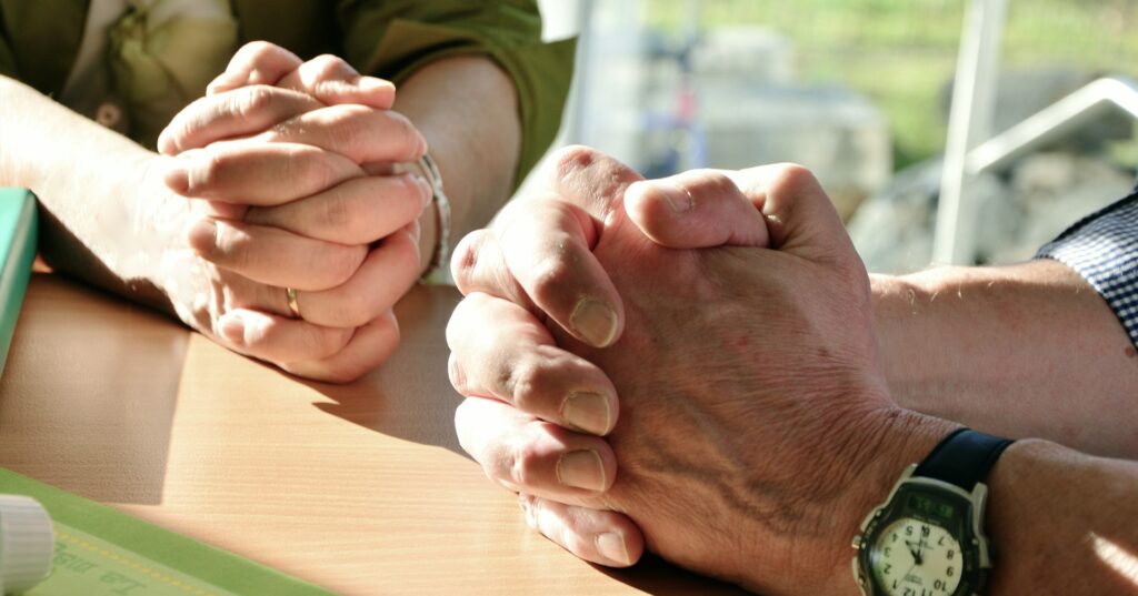 Hundreds of Christians in UK bless land for gigantic prayer monument The hands of two people are clasped and resting on a light colored wood table.