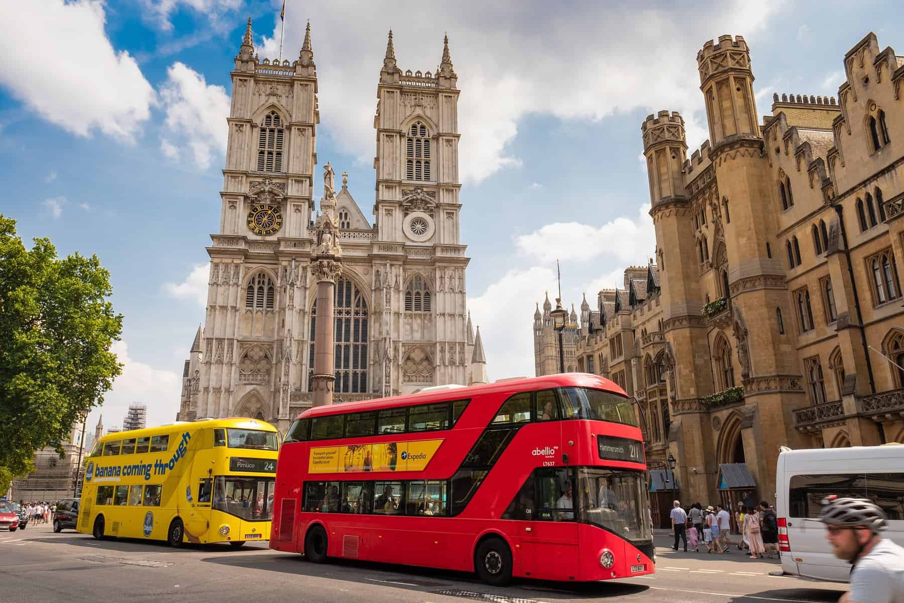 Two tour busses, one red, one blue, are driving down a street in London.