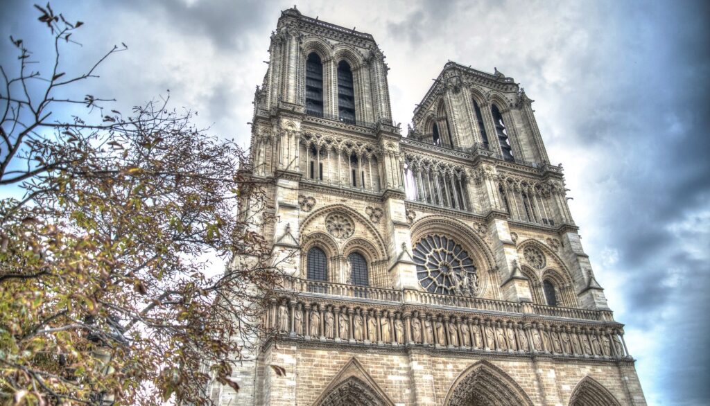 Towers of Notre Dame are seen from below at street level.