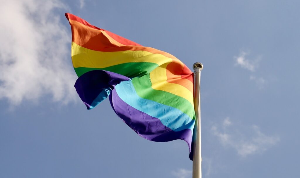 German Protestant pastor declares ‘God is queer’ during conference A rainbow Pride flag waves in the wind against a blue grey sky.