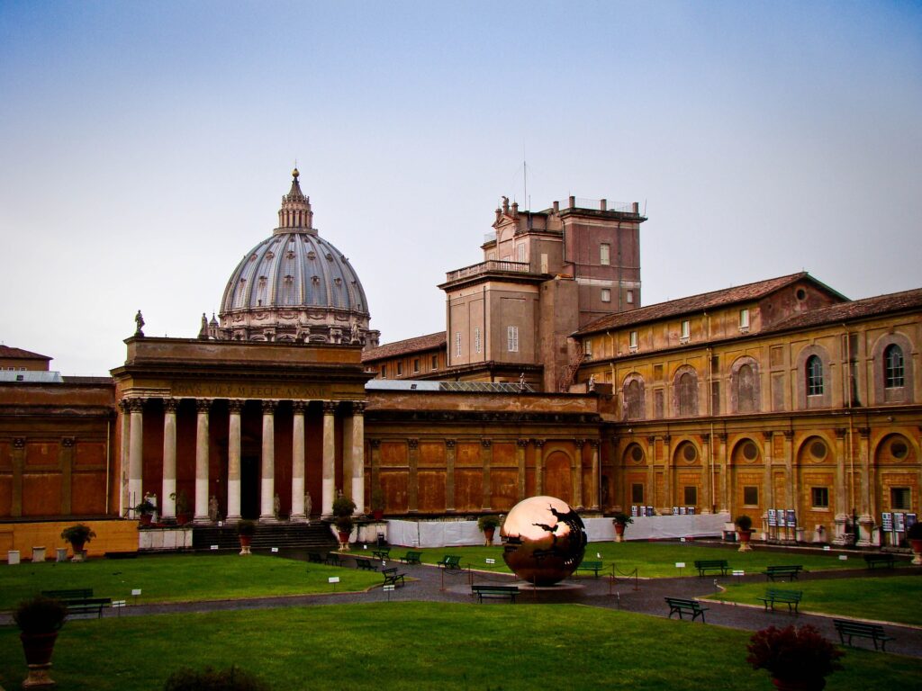 A view of the Vatican dome and surrounding buildings is seen from a distance.