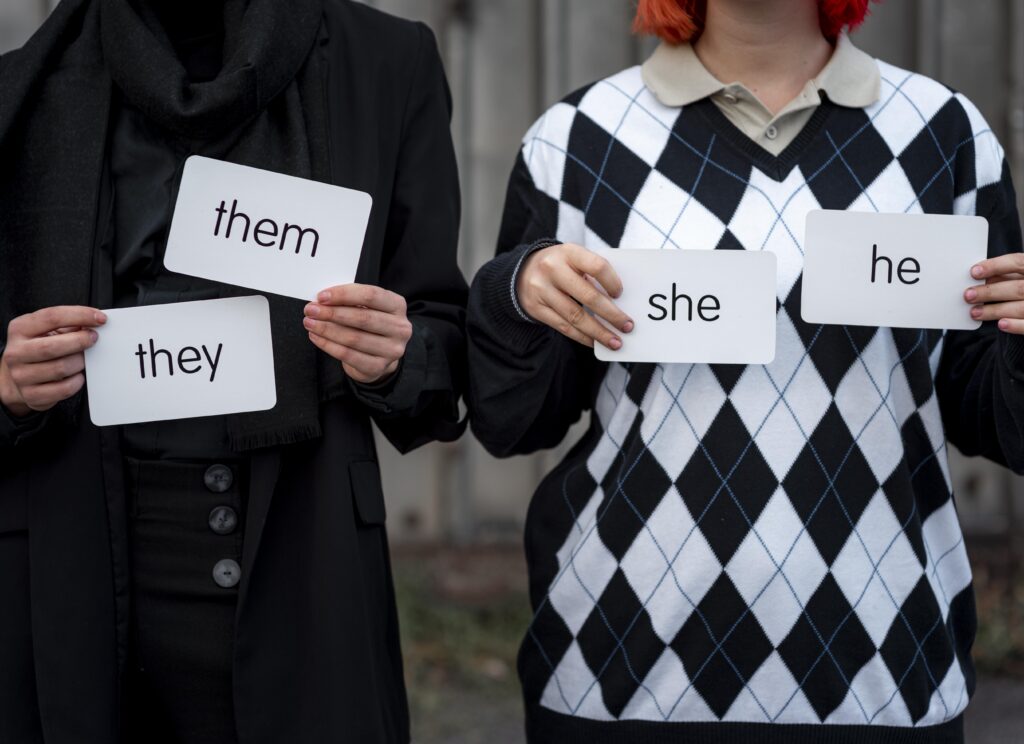 Employees fired for using their pronouns in emails The torso's of two people are seen close up and holding signs naming their pronouns.