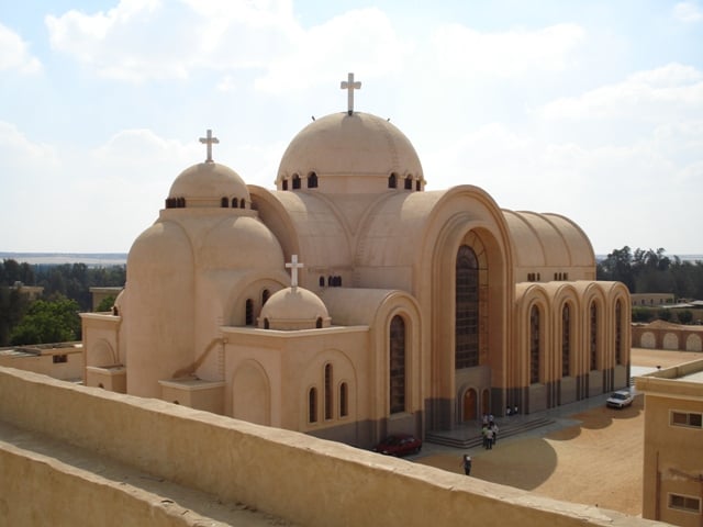 A sand colored and smooth surfaced Coptic monastery with domes and arches is shown.