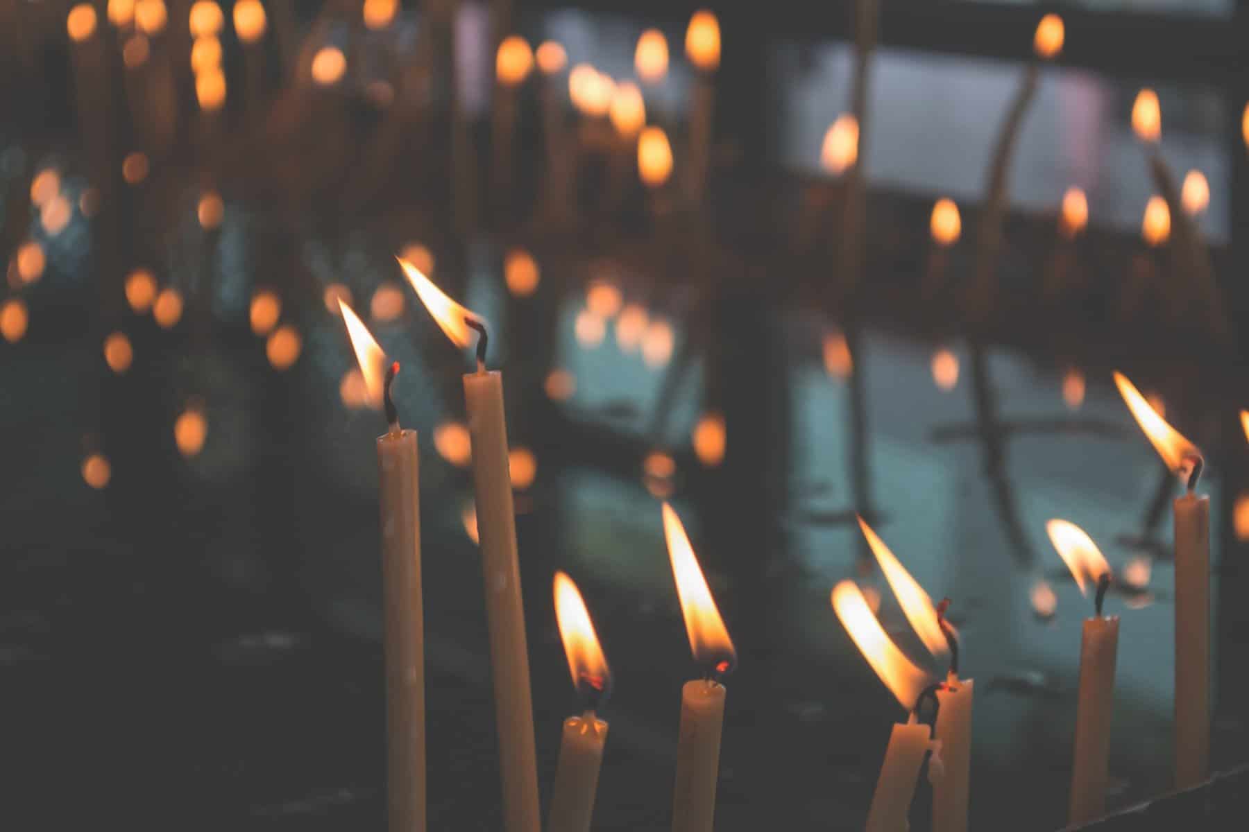 Lit tapered candles are seen in the foreground with lights twinkling behind them.