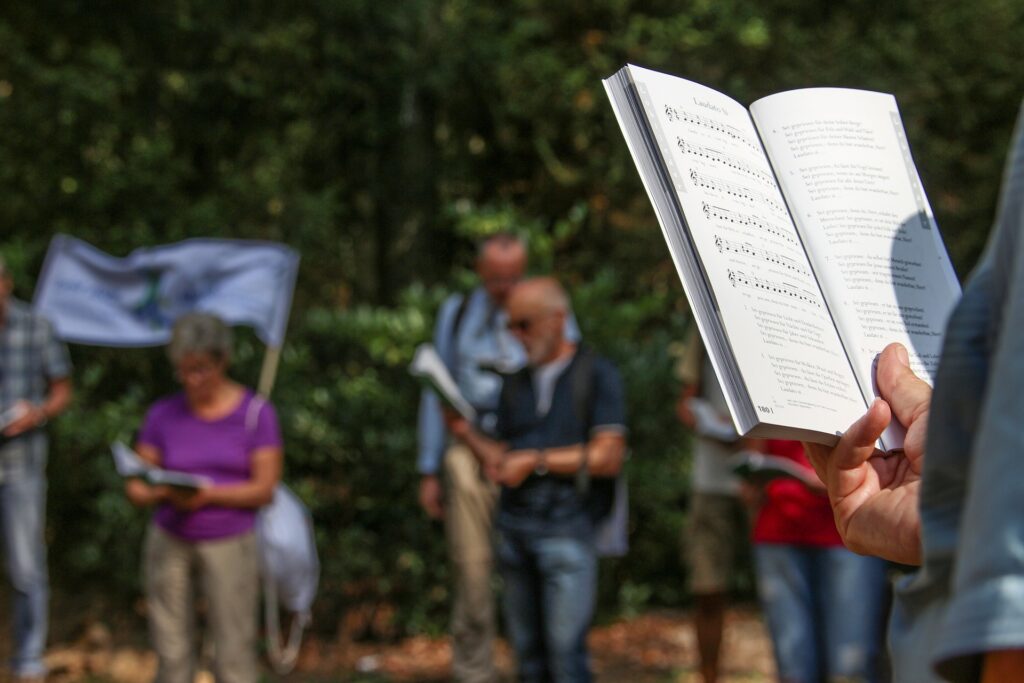 Idaho city to pay $300K settlement to singing Christians arrested during COVID-19 lockdowns A person holds a songbook in front of them at an outdoor gathering along with others.