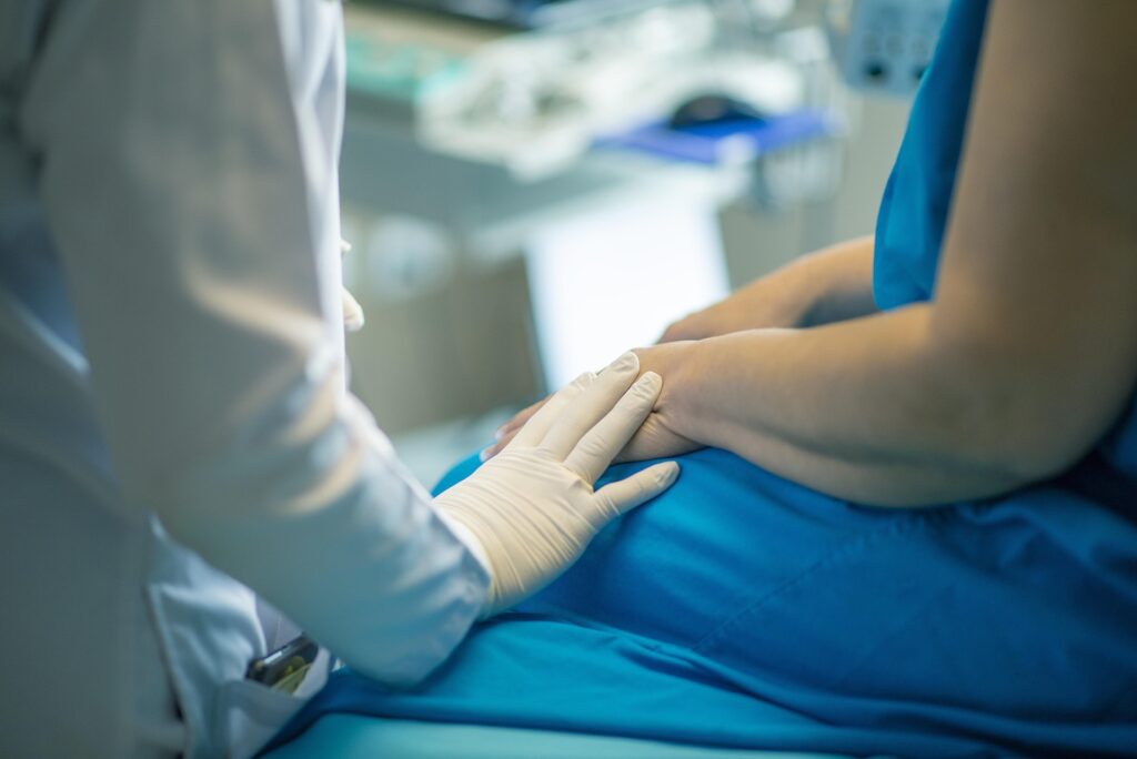 United Church of Christ encourages churches to assist 'pregnant people' in accessing abortions A woman sits on an exam table in a blue gown as the healthcare provider rests a hand on her arm.