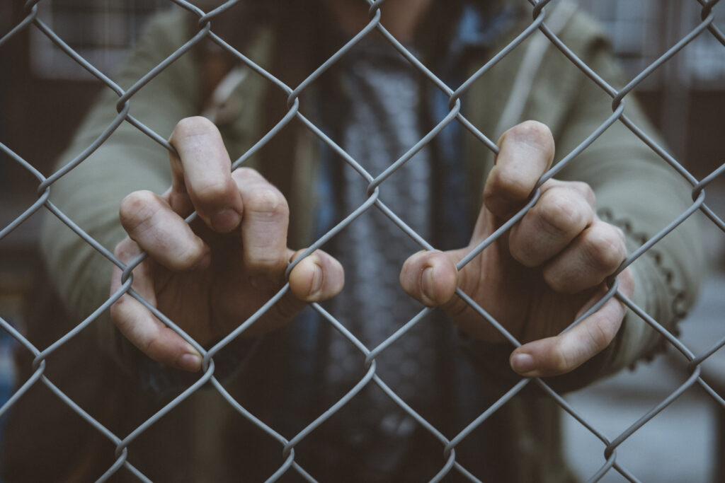 Young Christian Professionals help ex-convicts reintegrate Macro view of an urban person's hand on a chain link fence
