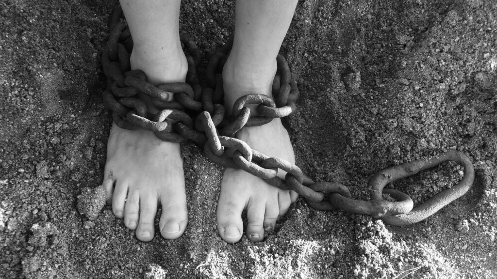 A light skinned person's feet are shown wrapped in heavy chains.