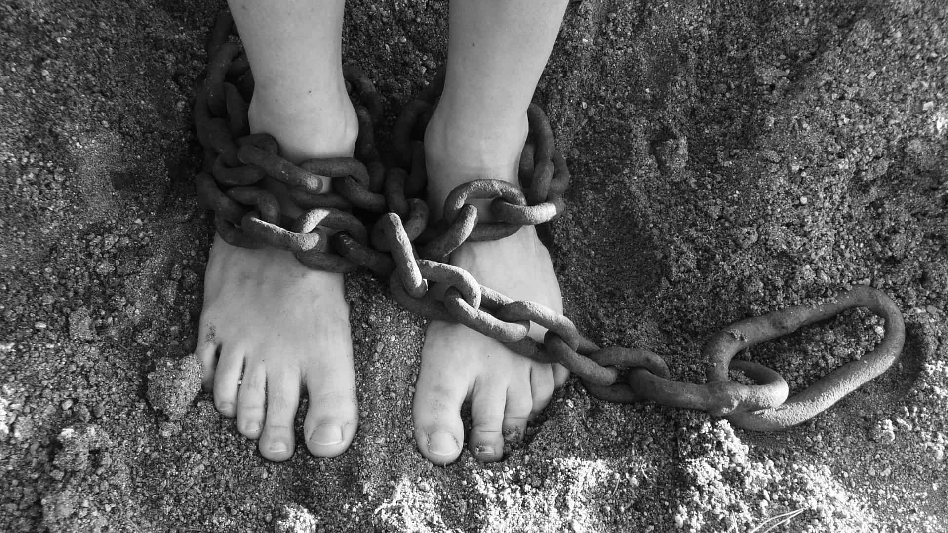 A light skinned person's feet are shown wrapped in heavy chains.