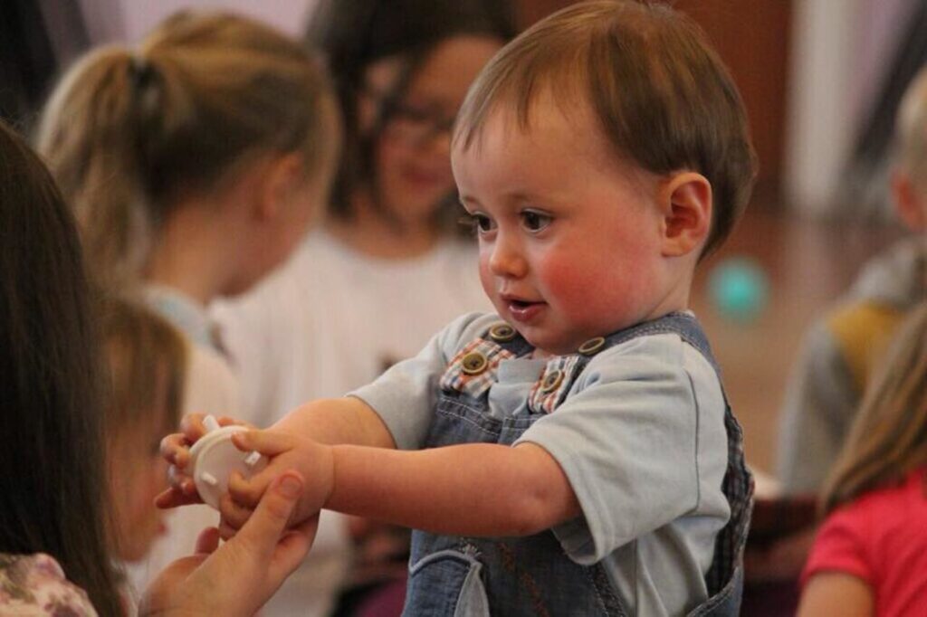 Denver archdiocese files lawsuit against Colorado over exclusion of Catholic schools A toddler holds an item out and arms length, showing it to someone.