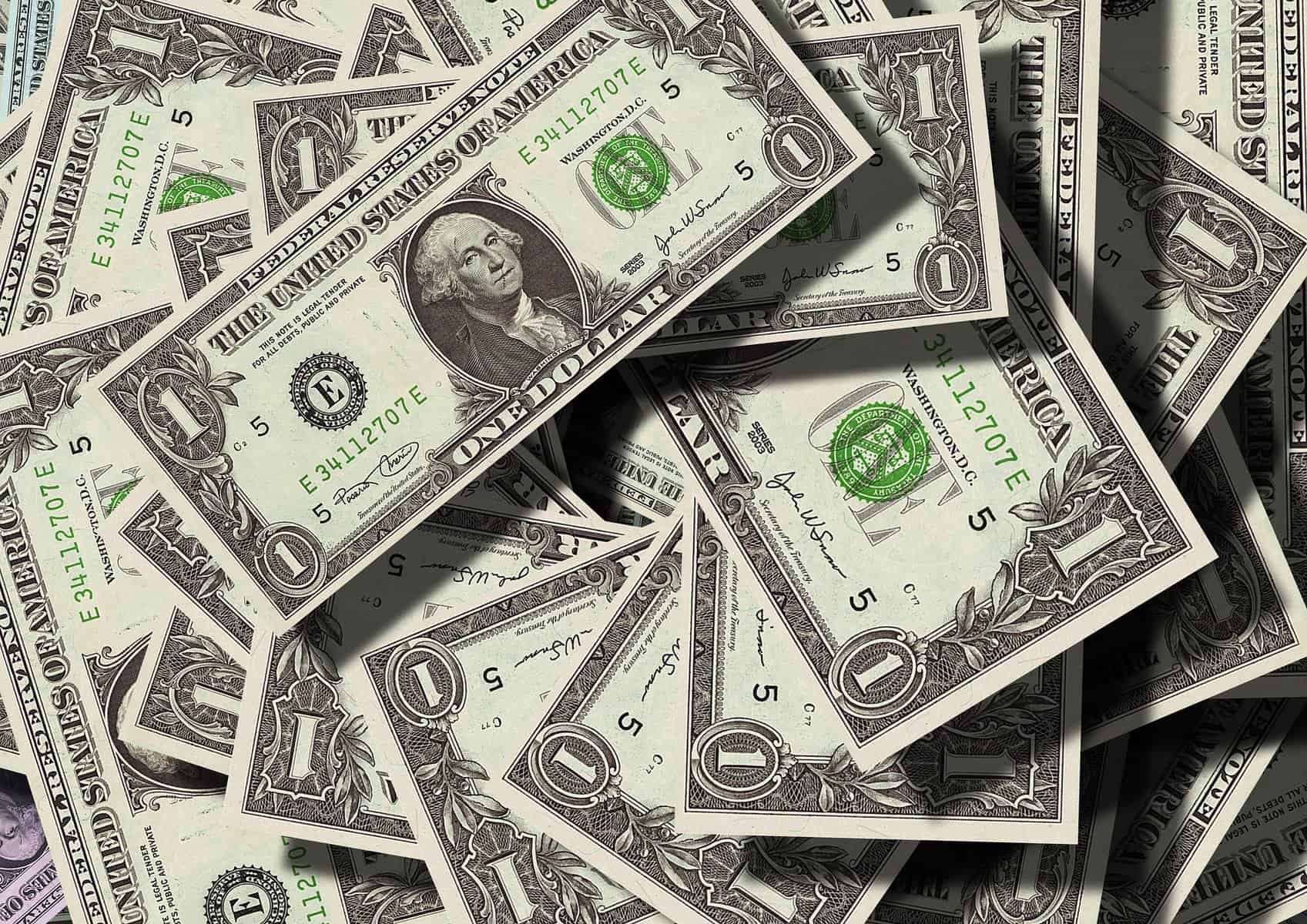 US dollar bills are loosely stacked in a pile and are shown from above.