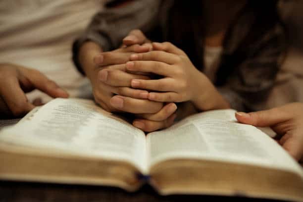Abuse at defunct sect was 'worse than anybody realises' Small hands are clasped and rest on an open bible while adult hands hold the bible's sides.