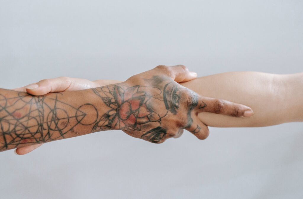 A tattooed hand and forearm is shown grabbing the forearm of a non-tattooed arm.